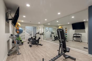 A well-equipped home gym with various exercise machines and a flat-screen TV mounted on the wall